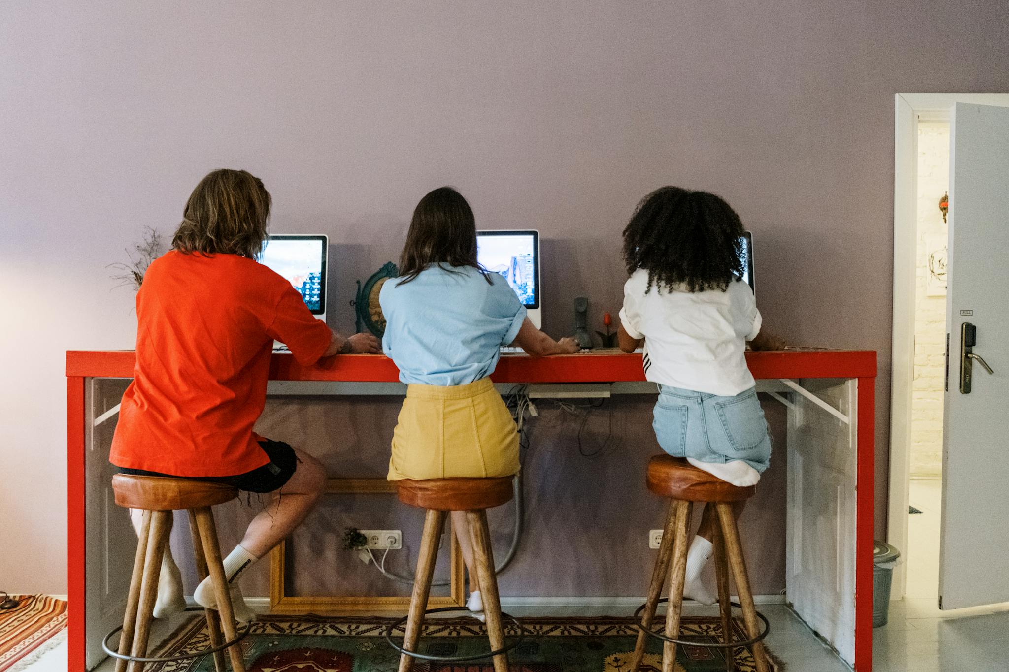 Three people working on computers in a modern indoor setting with wooden stools.